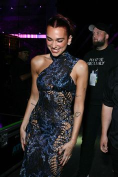 a woman in a blue dress standing next to a man at an event with tattoos on her arm