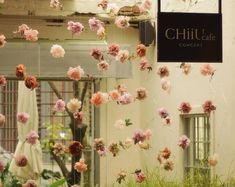 flowers are hanging from the ceiling in front of a building with chairs and tables outside