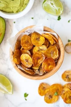 a wooden bowl filled with sliced bananas next to avocado and lime wedges