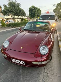 a red sports car parked on the side of the road next to a white van