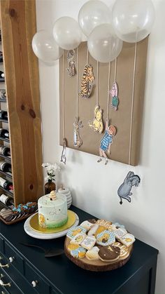 a table with cake, cookies and balloons hanging on the wall behind it is a wooden board that has pictures of winnie the pooh