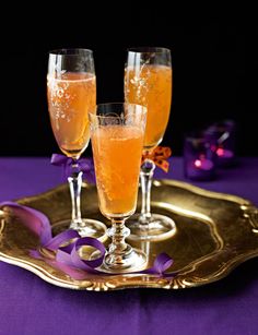 two glasses of champagne on a tray with purple ribbon around the rim and decorations in the background