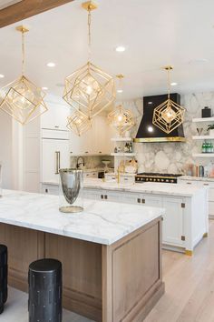 a large kitchen with marble counter tops and gold pendant lights hanging from the ceiling over the island