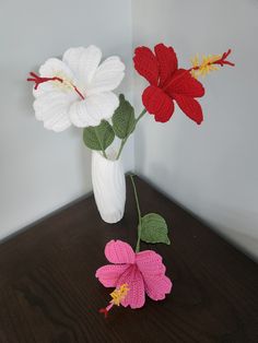 two crocheted flowers in a white vase on a wooden table next to each other