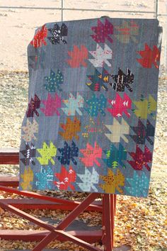 a quilt sitting on top of a red chair in the grass next to a fence