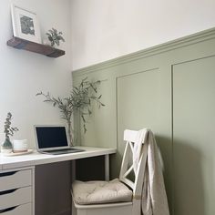 a laptop computer sitting on top of a desk next to a white chair and plant