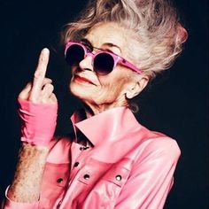 an older woman in pink is making the peace sign with her hand and wearing sunglasses