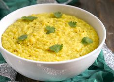 a white bowl filled with yellow food and garnished with cilantro leaves