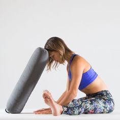 a woman sitting on the ground with her legs crossed and holding a yoga mat in front of her