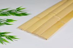 bamboo sticks are lined up next to some green leaves on a white table top,