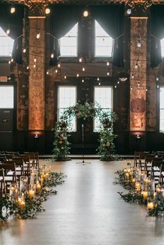 an indoor wedding venue with candles and greenery on the aisle, surrounded by windows