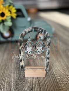 a pair of earrings is sitting on top of a wooden table next to a vase with sunflowers