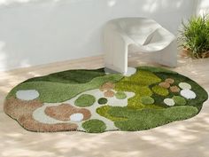 a green rug with flowers on it in a room next to a white chair and potted plant