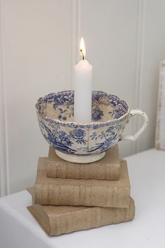 a candle is lit in a bowl on top of three stacked book pages, with a small white candle between two stacks of books