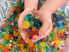 a child's hands holding a handful of gummy bears in a bowl filled with water