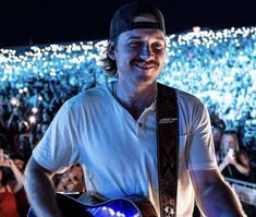 a man with a guitar standing in front of an audience at a music festival or concert