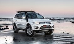 a white suv parked on top of a sandy beach next to the ocean at sunset