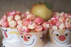 two cups filled with popcorn sitting on top of a white table next to an apple