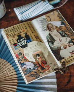 an open book sitting on top of a wooden table next to a fan and napkins