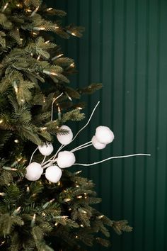 a christmas tree with white balls hanging from it's branches in front of a green wall