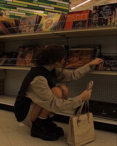 a woman sitting on the ground in front of a book shelf holding onto a purse