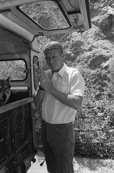 a black and white photo of a man standing next to a truck with his dog