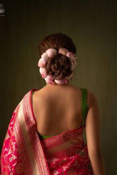 a woman wearing a pink and green sari with flowers in her hair, back view