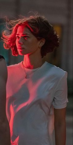 a woman with red hair is walking down the street at night, wearing a white t - shirt