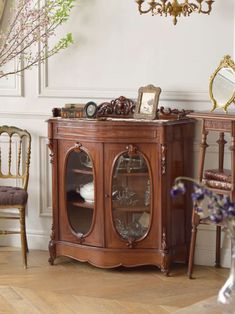 a wooden cabinet with glass doors in a living room next to two chairs and a table