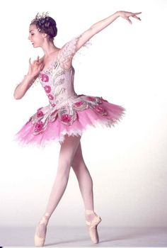 a ballerina in pink and white is posing for the camera with her arms outstretched