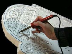 a person holding a pen and drawing on a large piece of paper with intricate designs