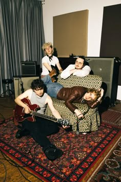 three men sitting on a couch with guitars in their hands and one man playing the guitar