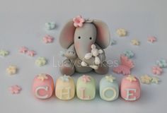 a small elephant sitting next to some letters and flowers on a white surface with pastel colors