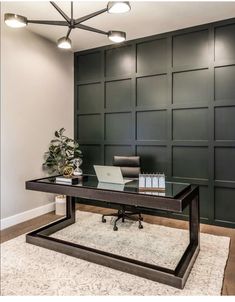 a desk with a laptop on it in front of a green paneled office wall