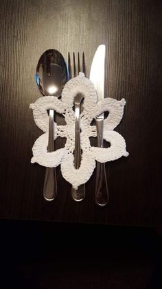 a fork, knife and spoon on a table with white crocheted napkins