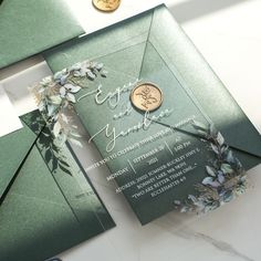 a green and gold wedding card on top of a white table with some coins next to it