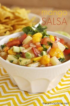 a white bowl filled with salsa next to some tortilla chips on a yellow and white table cloth