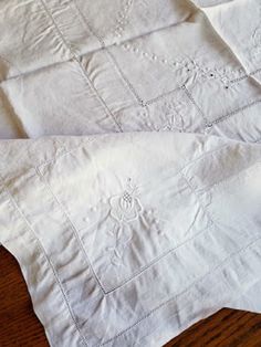 two white linen napkins sitting on top of a wooden table next to each other