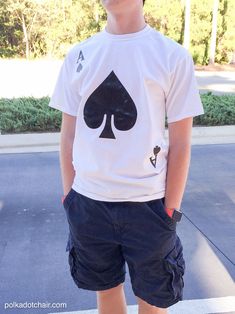 a young man standing on the sidewalk wearing shorts and a t - shirt with a ace symbol