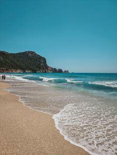 two people are walking along the beach near the water's edge with waves coming in