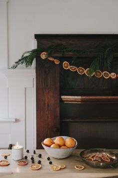 a bowl of oranges sitting on top of a table next to a fireplace with candles