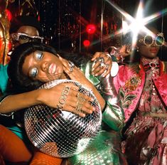 a woman laying on top of a disco ball in front of two other people wearing costumes