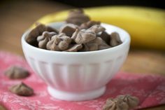 a white bowl filled with chocolate chips on top of a pink napkin next to a banana