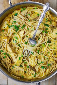 a large pot filled with pasta and chicken on top of a wooden table next to a fork