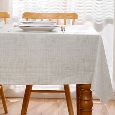 a table with a plate on it in front of a white curtain and wooden chairs