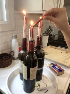 a person lighting candles on top of three wine bottles in front of a kitchen counter