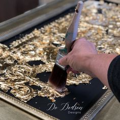 a person is painting gold leaf designs on a metal tray with a paintbrush in their hand