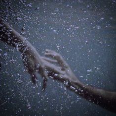 two hands reaching out from the water to grab something with their fingertips, while it is raining