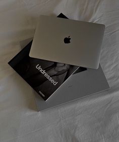 two apple laptops sitting on top of each other in front of a white sheet