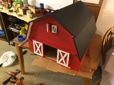 a red barn model sitting on top of a table next to tools and other items